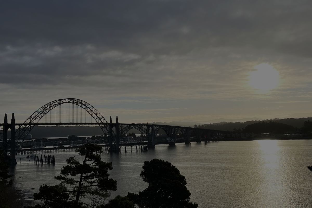 Arched Yaquina Bay Bridge over the bay, with the sun low over the water
