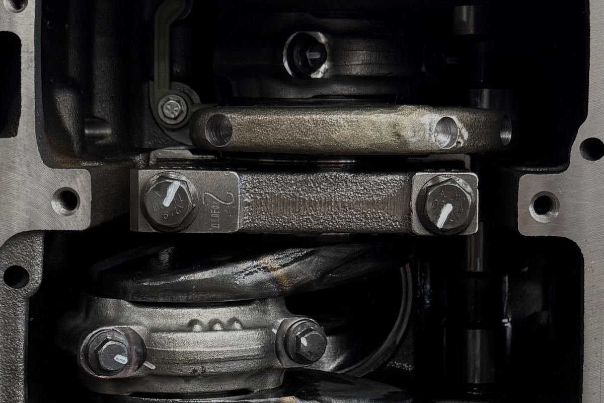 A close-up from below of the crankshaft, a main bearing cap and a connecting rod