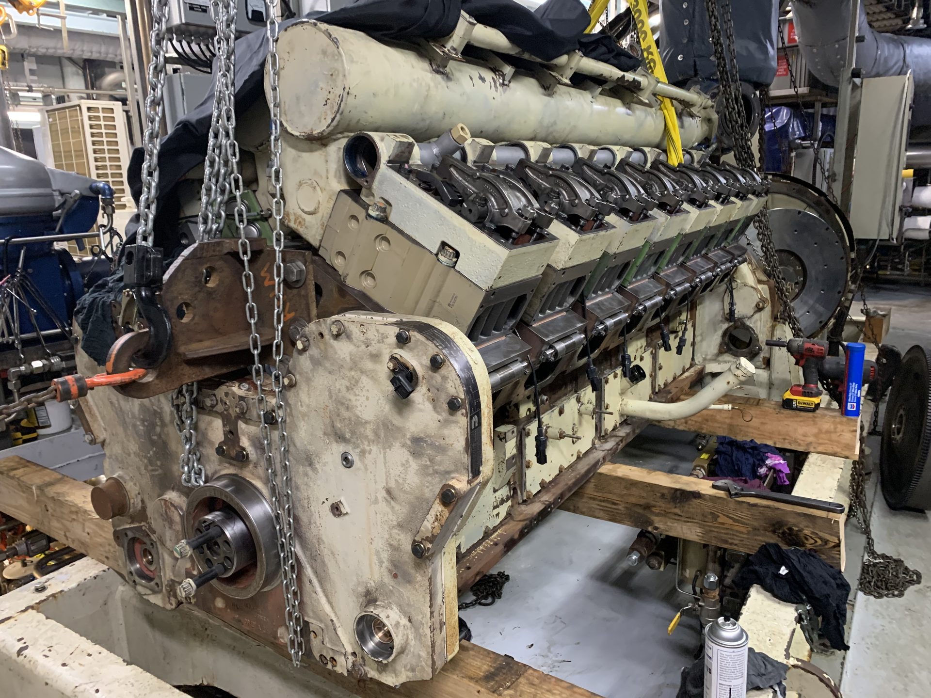 Large V-block diesel engine on wooden cribbing in an engine room, partly torn down and rigged with lifting chains